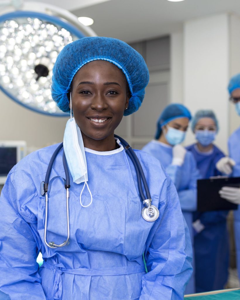 Portrait of happy African American woman surgeon standing in operating room, ready to work on a patient. Female medical worker in surgical uniform in operation theater.
